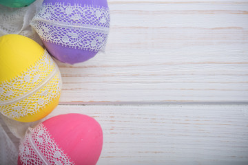 easter eggs with lace ribbon on white wooden background