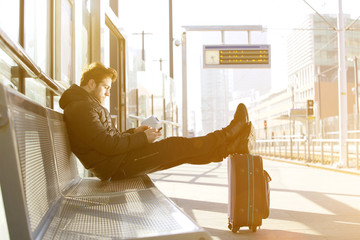 Young man waiting at train station platform with mobile phone