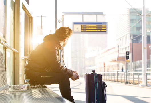Young man sitting at train station looking at time schedule