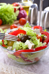 Greek salad in glass dish with fork and vegetables background