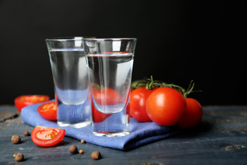 Glasses of ouzo and tomatoes on wooden table, on grey