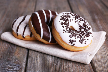 Delicious donuts with icing on napkin on wooden background