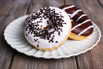 Delicious donuts with icing on plate on wooden background