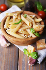 Raw pasta in bowl with cheese and vegetables on table close up