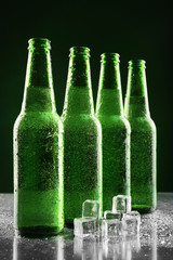 Glass bottles of beer with ice cubes on dark background