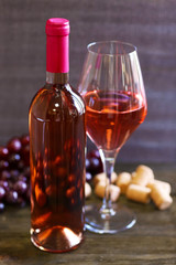 Bottle and glass of rose wine on wooden table on gray