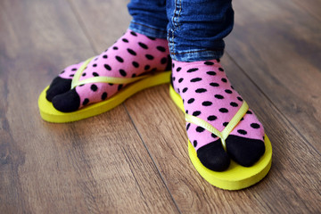 Female feet in socks with pink flip-flops, on floor background