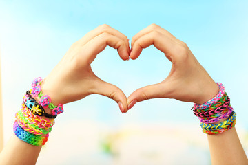 Female hands in shape of heart with bracelets on color blurred background
