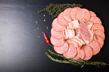 Slices of sausage and bacon on a round cutting board with rosema