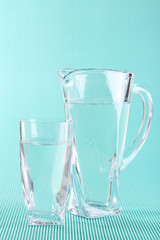 Glass pitcher and glass of water on blue background