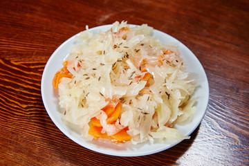 On the wooden table is a white plate with a salad of pickled cab