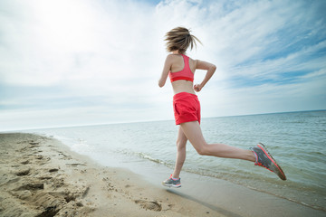 Fototapeta na wymiar Young lady running at the sunny summer sand beach. Workout. Jog
