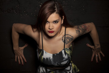 pretty young woman with tattoos posing in a dress on a black