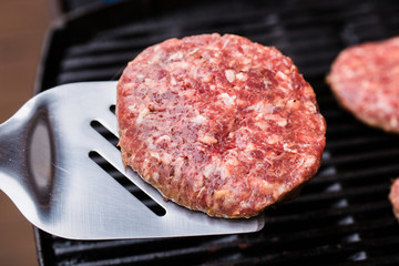 Grilled ground beef pattie burger on spatula against BBQ