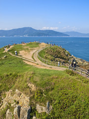 Fototapeta na wymiar green hill by sea with people walking along paths