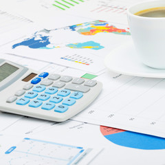 Coffee cup and calculator over different charts - close up shot