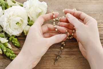 Woman holding wooden rosary in hands.