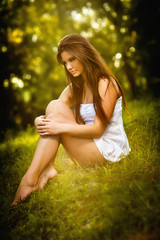 Naklejka na ściany i meble Attractive young woman in white short dress sitting on grass 