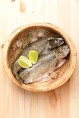 Raw trout fish with ice in wooden bowl. top view