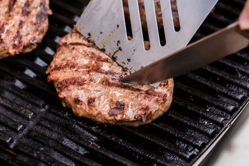 Grilled ground beef pattie burger with spatula and knife on BBQ