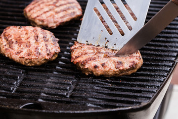 Grilled ground beef pattie burger with spatula and knife on BBQ