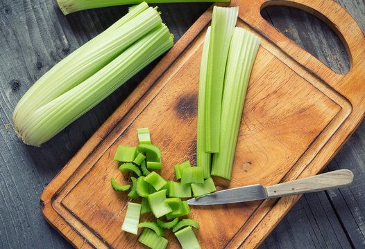 Fresh green celery stems on wooden cutting board closeup