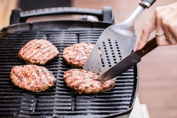 Grilled ground beef pattie burger with spatula and knife on BBQ