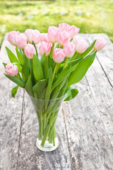 bouquet of light pink tulips on the oak brown table in a clear g