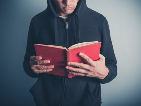 Young man in hooded top reading red book