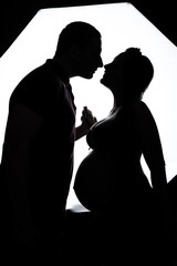 Silhouette of a husband and pregnant wife against the window