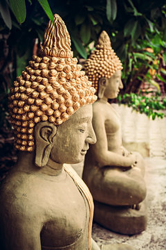 Sitting stone Buddha statues at temple area among green foliage