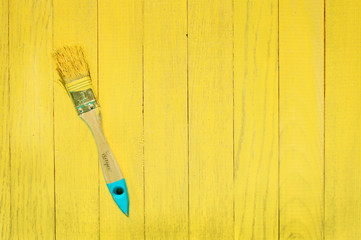 Brush in yellow paint on yellow wooden background