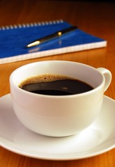 Coffee on a Desk, with Notebook and Pen in the Background