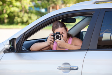 Young woman taking picture with camera throuth the car window