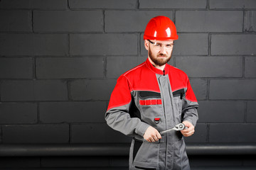 man wearing overalls with red helmet and wrench near brick wall