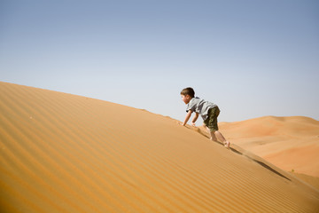 Young boy plays among sand dunes in desert