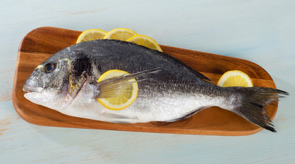 Raw sea bream with lemon on  wooden cutting board.