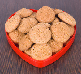 Oatmeal cookies in a red heart plate on a brown surface