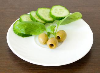 Slices of fresh cucumber, olives, basil leaves on a white plate
