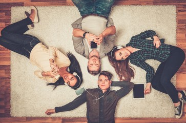 Happy multiracial friends relaxing on a carpet with gadgets
