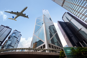 Tall city buildings and a plane flying overhead - obrazy, fototapety, plakaty