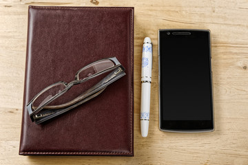 Notebook, pen and phone with blank screen on the table