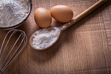 spoon bowl with flour eggs corolla on wooden board food and