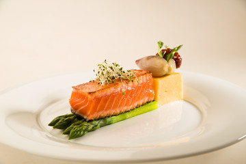 A piece of fried salmon, asparagus and corn porridge on a white