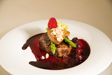 Piece of roasted meat in cherry sauce, asparagus  and raspberry