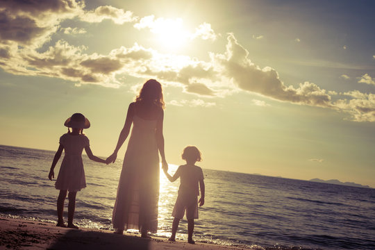 Mother and children standing on the beach at the sunset time.