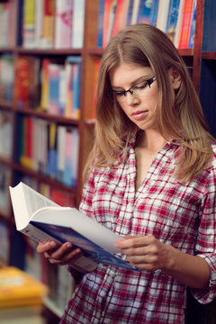Portrait Of Teenage Student Reading Book In Library Class