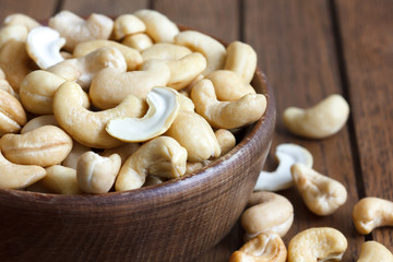 Wooden bowl of cashew nuts from above. On dark wood.
