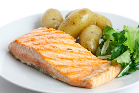 Grilled fillet of salmon on plate with green salad and potatoes.