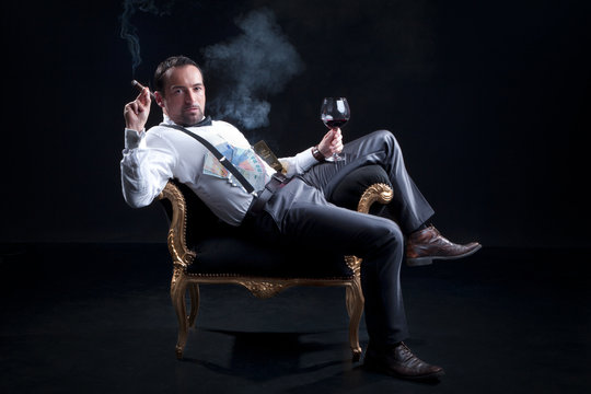 Reicher Businessmann im Hocker mit Zigarre und Weinflasche lässig Porträt